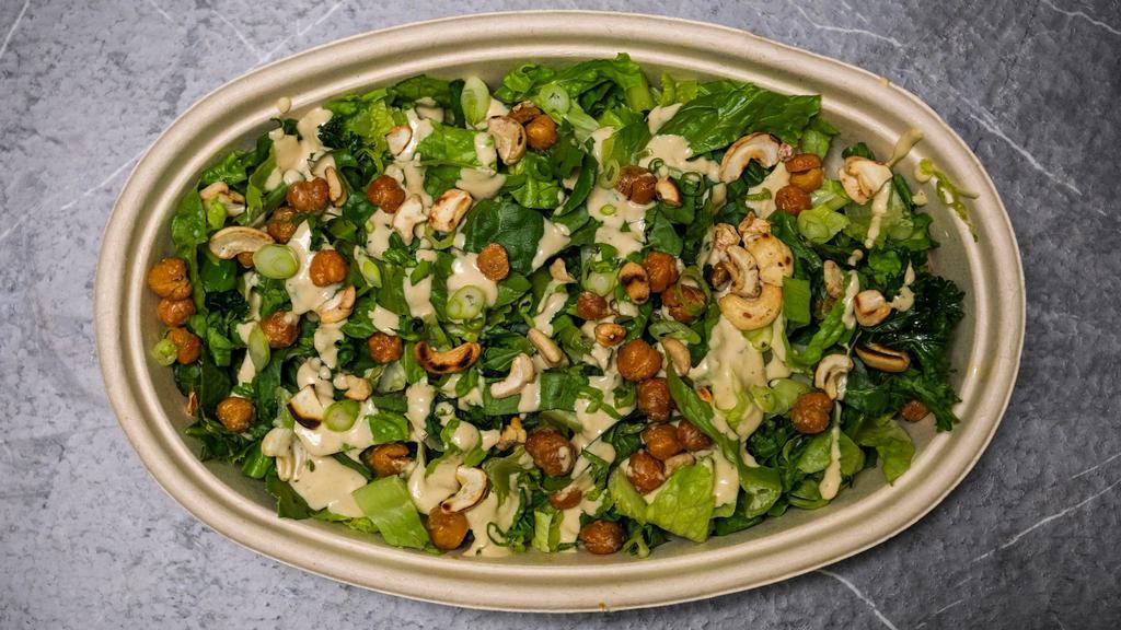 Kale Cashew-Caesar Salad · Baby kale, toasted cashews, crispy chickpeas, scallions, and cashew Caesar dressing. Vegan, Gluten-Free, Dairy-Free, Soy-Free, Contains Cashews