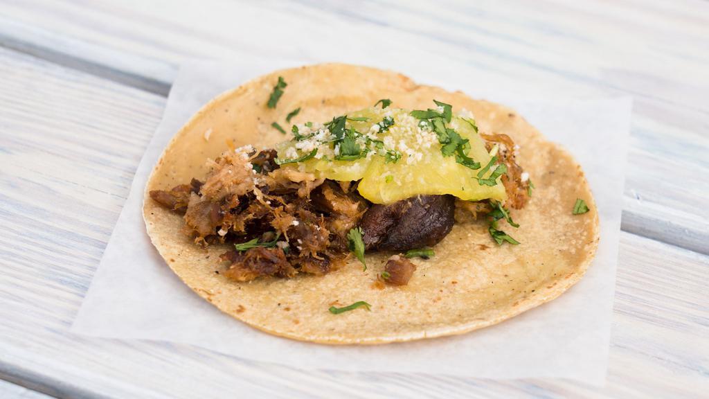 Pork And Pineapple · Citrus roasted pork, garnished with pineapple, chicharron and cilantro on a corn tortilla
