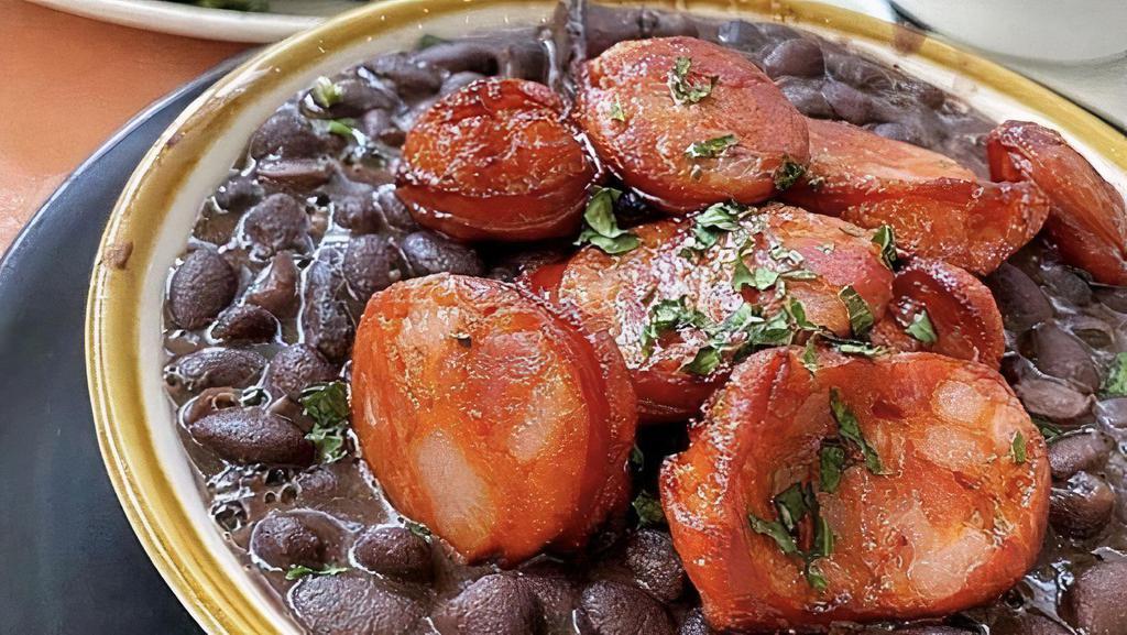 Feijoada Do Santo · Brazilian slow cooked black bean & pork stew, with dried meats and sausage, served with white rice,  sautéed collard greens orange slices and farofa (toasted yucca flour)