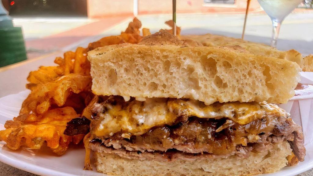 Pirate Rib Eye Steak Sandwich · Thin sliced rib eye is grilled and topped with cheddar, caramelized onions and mushrooms and finished off with pirate pale horseradish blue cheese sauce. Served with fries and a house made pickle.