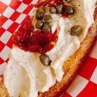 Hummus Toast · Hummus spread on sourdough bread with sundried tomatoes, capers & EVOO drizzle.
