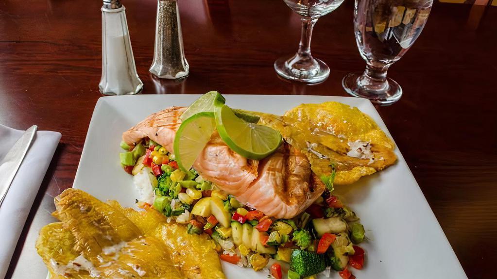 Salmon A La Parrilla · Fresh grilled salmon on a bed of sautèed broccoli, asparagus, basil, green squash, yellow squash & rice. Served with tostones lightly glazed in a garlic bacon sauce.