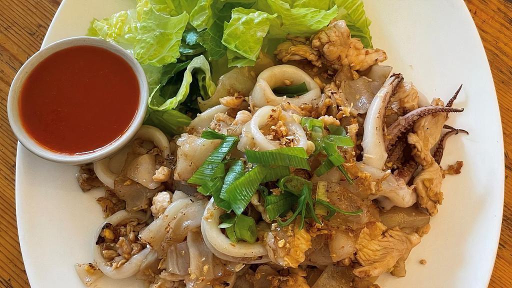 Guay Tiew Kua · Wok-fried flat noodles with eggs on a bed of romaine lettuce served with a side of Sriracha sauce