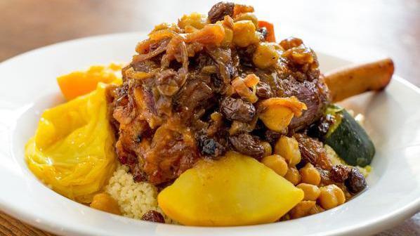 Lamb Shank Couscous · slow-cooked lamb shank, braised butternut squash, carrots, zucchini, celery, turnips, served over a bed of fluffy couscous, topped with chickpeas, raisins, & caramelized onions