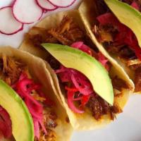 Tacos De Cochinita Pibil · Braised pulled pork cooked with achiote, topped with avocado, pickled habanero red onions, a...