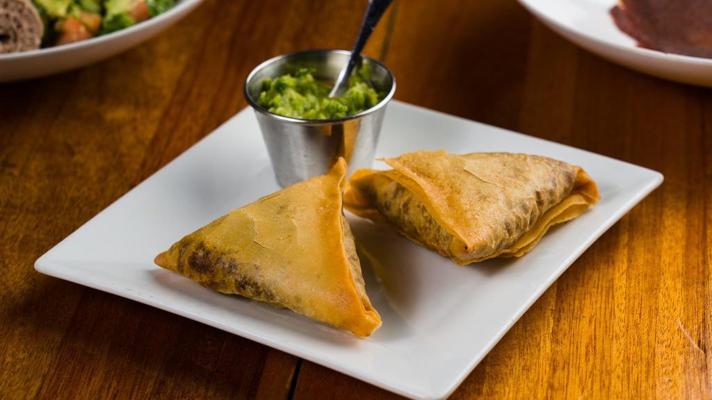 Sambusa (Dinner) · Two triangular pastries stuffed with lentil and pepper mix and served with a spicy cilantro sauce.