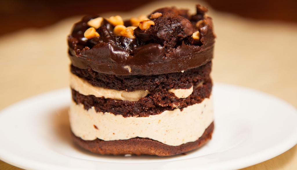 Peanut Butter Explosion · Brownie bottom, layers of velvety peanut mousse, chocolate genoise, topped with peanut butter chips, brownie bits, drizzled in fudge.