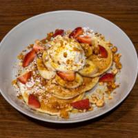Buttermilk Pancakes · Three buttermilk pancakes with sliced bananas & strawberries, honeycomb and toasted hazelnut...