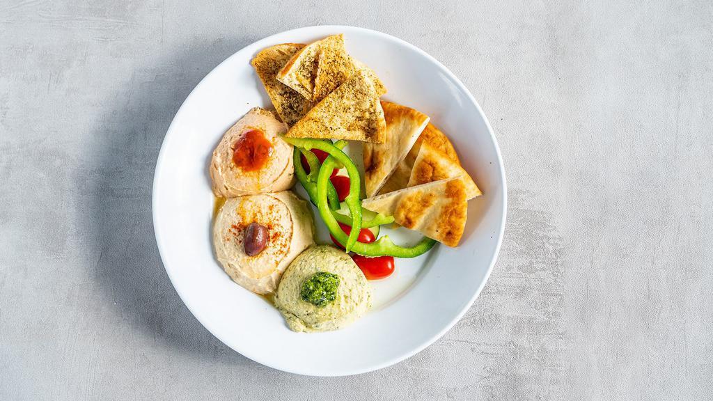 Hummus Trio · Basil Pesto, Spicy, and Classic Hummus paired with pita bread, pita chips, cucumbers, bell peppers, and grape tomatoes.