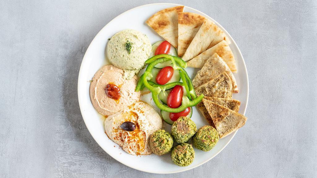 Hummus Trio With Falafel · Basil Pesto, Spicy, and Classic Hummus paired with falafel, pita bread, pita chips, cucumbers, bell peppers, and grape tomatoes.