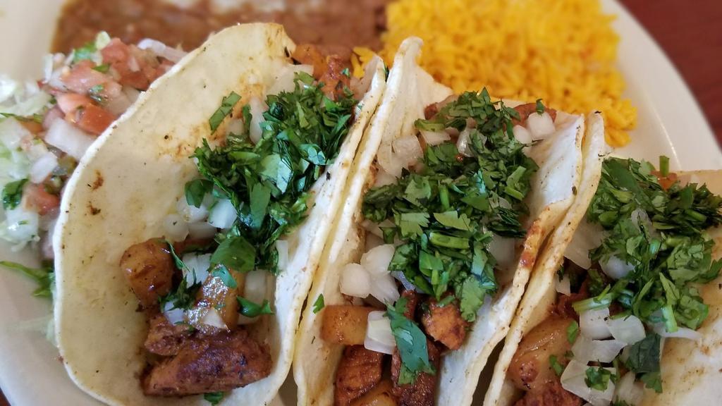 Tacos Al Pastor · Specially marinated strips of pork grilled with pineapples. Topped with cilantro and onions. Served with rice and beans on the side.