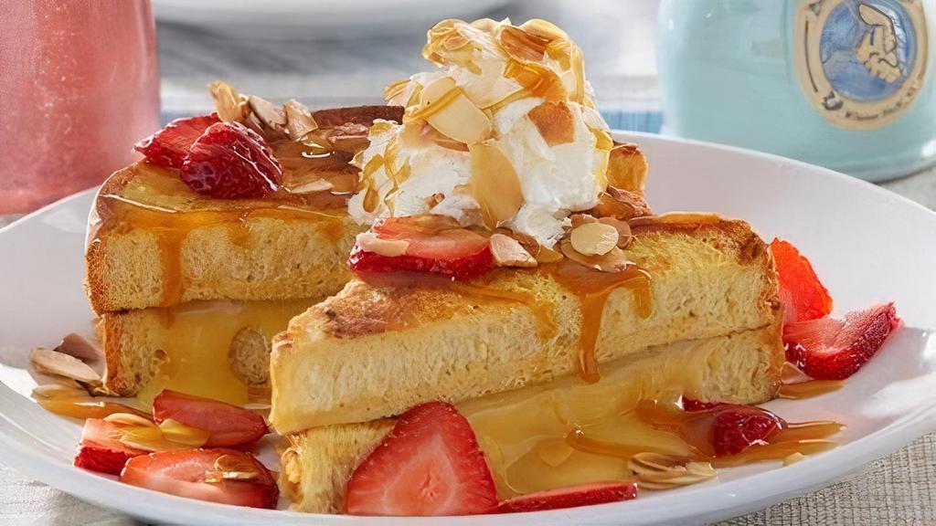 Lemon Custard Stuffed French Toast · French toast stuffed with lemon custard, topped with fresh strawberries, fresh whipped cream, toasted almonds and salted caramel. Served with two eggs any style and baked bacon or house-made sausage patties.