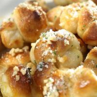Fried Mini Garlic Knots · Our pizza dough rolled and tied into knots, fried, then smothered in melted butter and fresh...
