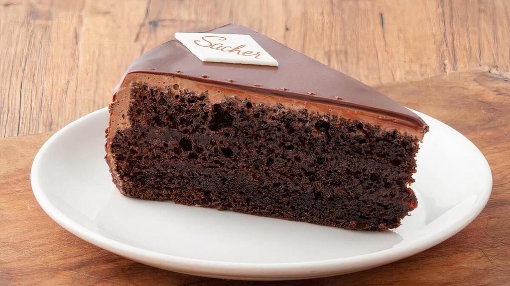 Sacher Torte · Our Sacher Torte with three chocolate cake layers soaked with vanilla syrup and filled with a thin layer of raspberry jam finished with chocolate mousse topping.  Enrobed in rich chocolate ganache and topped with our traditional Sacher candy emblems.