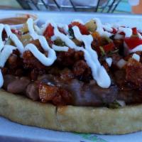 Huarache Al Pastor · Fried masa topped with al pastor (marinated pork), refried beans, pineapple salsa, sour crea...