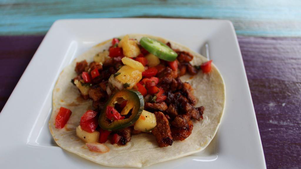 Pineapple Al Pastor Taco · Al pastor (marinated pork), pineapple salsa, and bread and butter jalapeños and onions. Served in a flour tortilla.