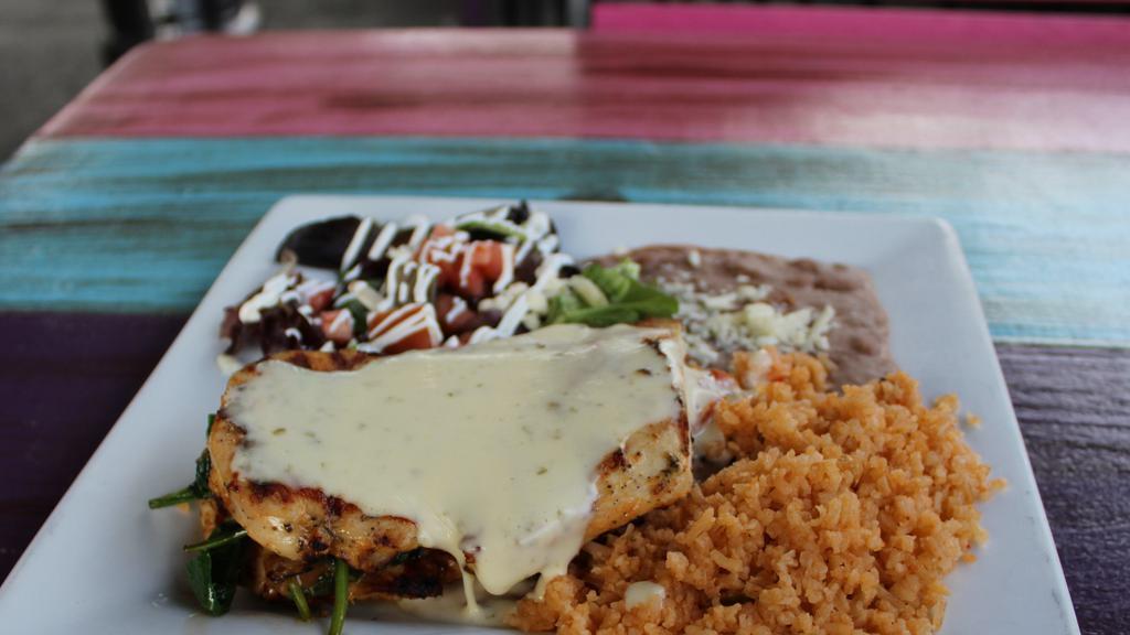 Pollo Relleno · Marinated grilled chicken breast topped with spinach, fresh lime pico de gallo, and queso dip. Served with a side of rice, refried beans, side salad (lettuce, sour cream, tomatoes, queso fresco), and flour tortillas.