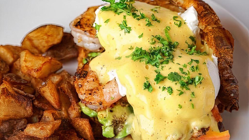 Cajun Shrimp Benedict · Open faced croissant topped with shrimp, avocado, tomato, pickled onions, 2 poached eggs and hollandaise sauce on the side.. Served with breakfast potatoes.