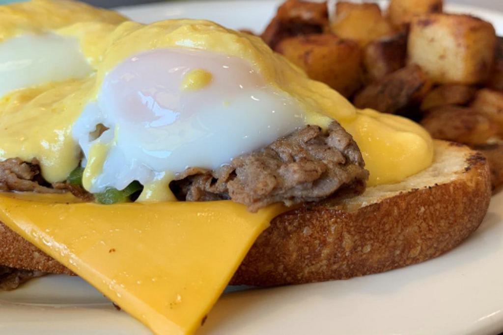 Philly Cheese Steak Benedict · Thinly-sliced steak, American cheese, onions and peppers on garlic toast, topped with two poached eggs and hollandaise sauce.