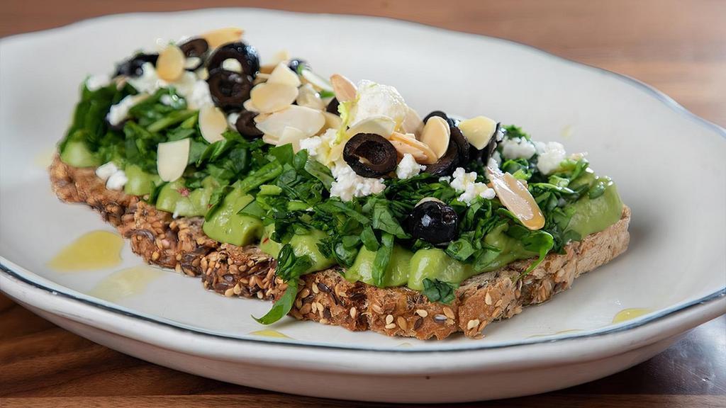 Greek Avocado Toast · Multigrain Toasted Bread, Avocado spread, Spinach, Feta Cheese, Black Olives, topped with Roasted Almonds, Herbs de Provence and drizzled with Olive Oil.