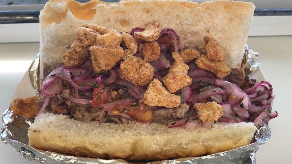 Sanduche De Chancho (Pulled Pork Sandwish) · Pulled pork inside a fresh Cuban bread topped with pork cracklings and pickled onions.