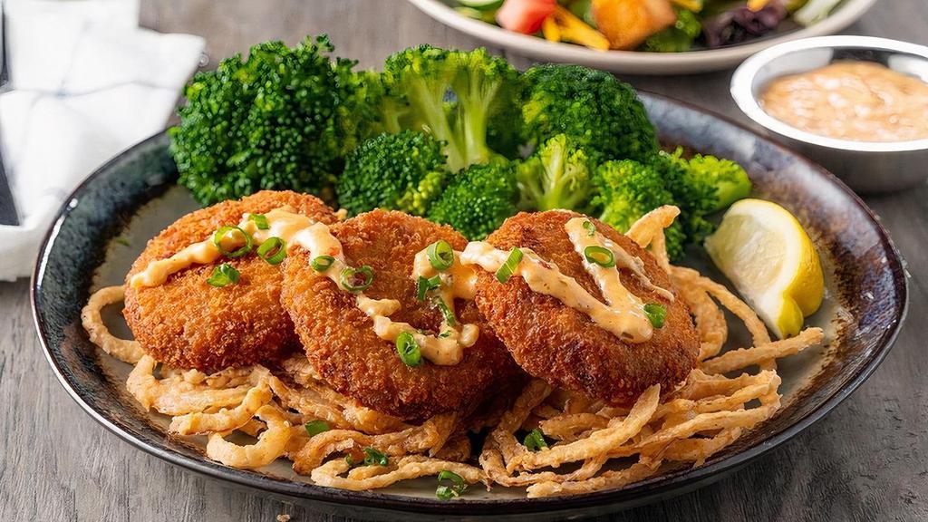 Crispy Crab Cakes · Three lightly fried crab cakes served over crispy onions with a side of creamy Cajun sauce.