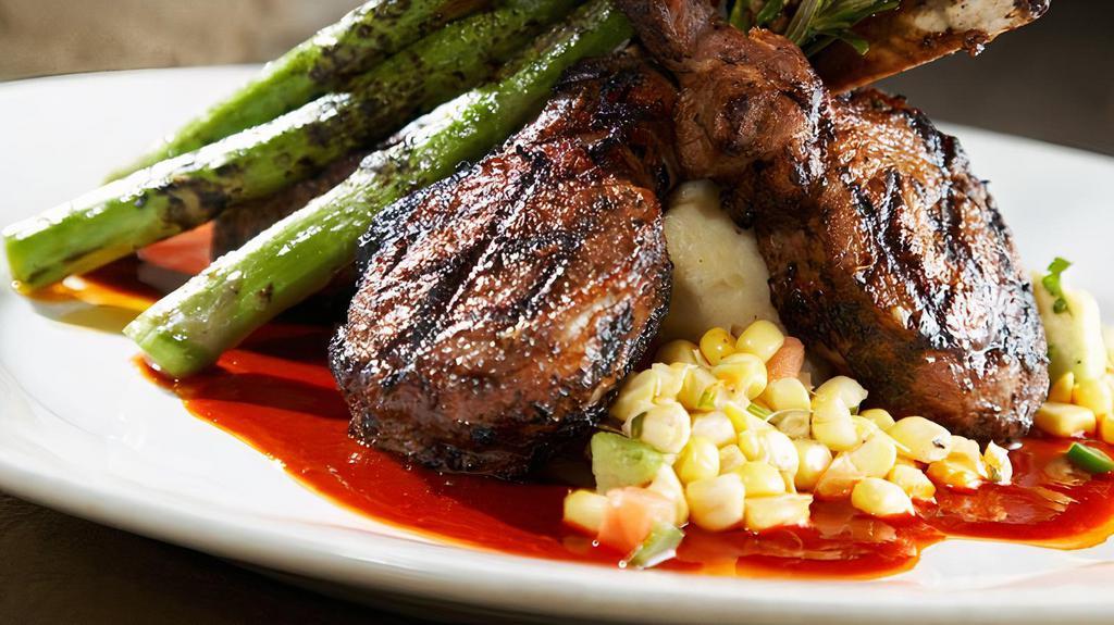 New Mexican Rack Of Lamb · Fresh chile and herb rubbed lamb rack grilled over a New Mexico guahillo red chile puree, served with yukon gold mashed potatoes, grilled asparagus and garnished with a cool corn relish and cilantro leaves.