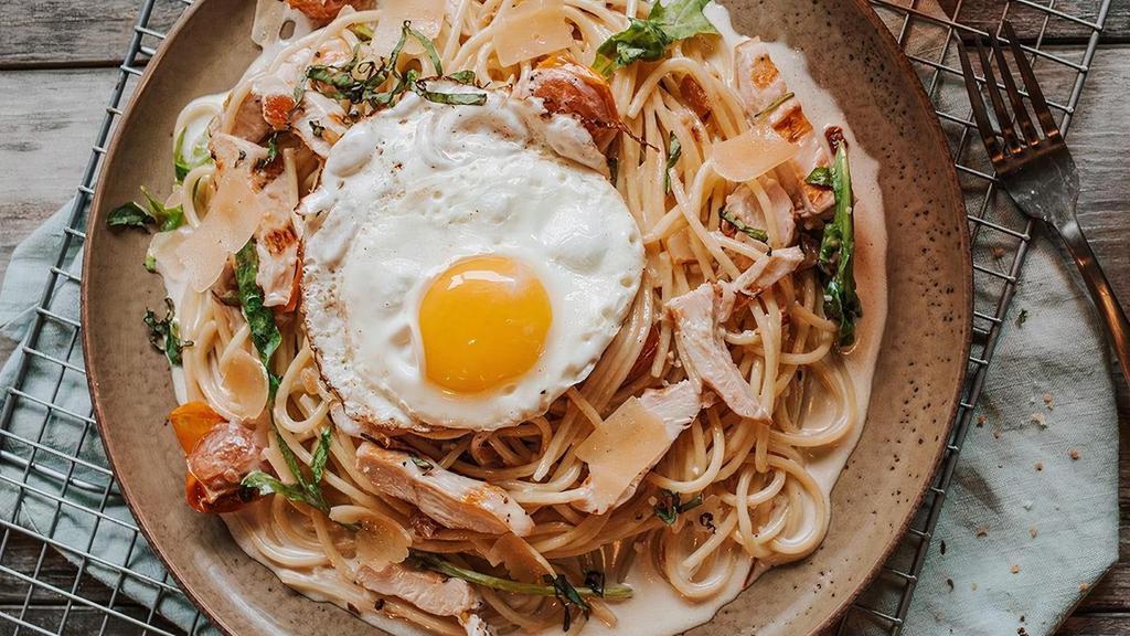 Chicken Carbonara · Spaghetti tossed with garlic parmesan cream sauce,  blistered tomatoes, basil, arugula, black peppercorn, and bacon topped with a fried egg.
