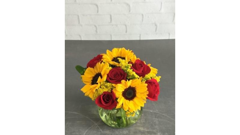 Sundrops · Send someone some sunshine with Sundrops! You can’t go wrong with sunflowers, red roses, solidago & greens designed in a darling glass vase! Occasional substitutions of equal or greater value of flowers, colors, or vases may occur due to supply chain limitations.