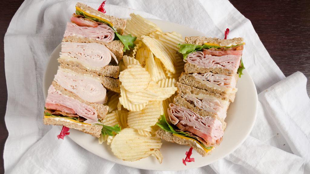 Deli Club Box · Ham and roasted turkey breast, Swiss and cheddar cheese,  bacon, leafy lettuce, and tomato on multigrain wheat bread. Served with chips and pickle and 1 dessert choice: Brownie, Chocolate Chip Cookie, or Cranberry Walnut Oatmeal Cookie.