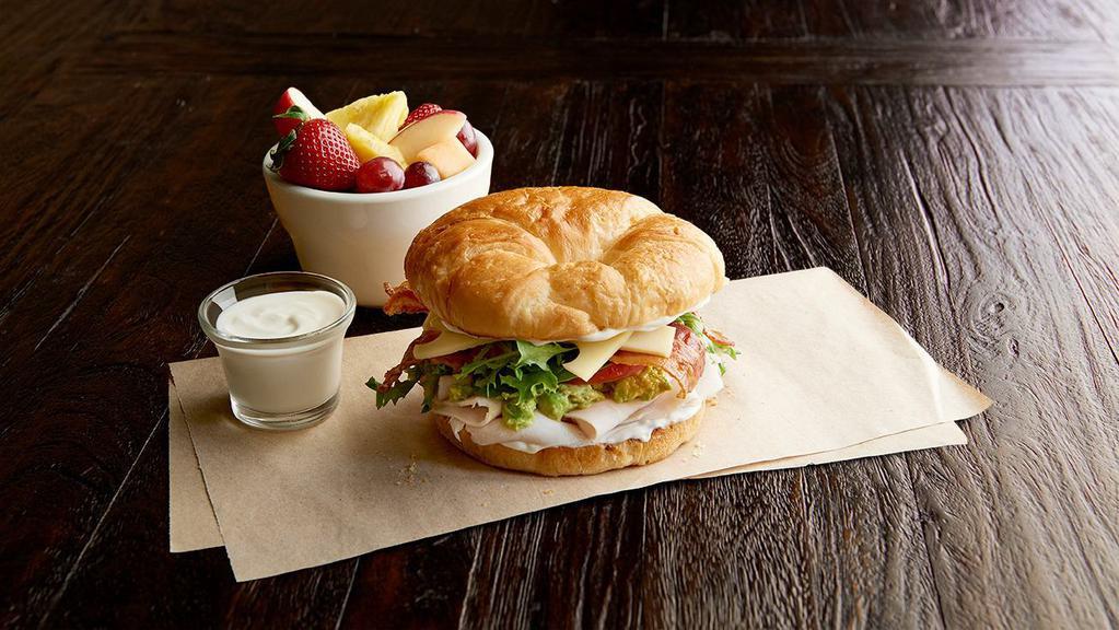 California Club Regular · Roasted turkey breast, bacon, Swiss, guacamole, tomato, organic field greens, mayo, on a toasted croissant. Choice of one side: fresh fruit, steamed veggies, baked chips or blue corn chips with salsa.