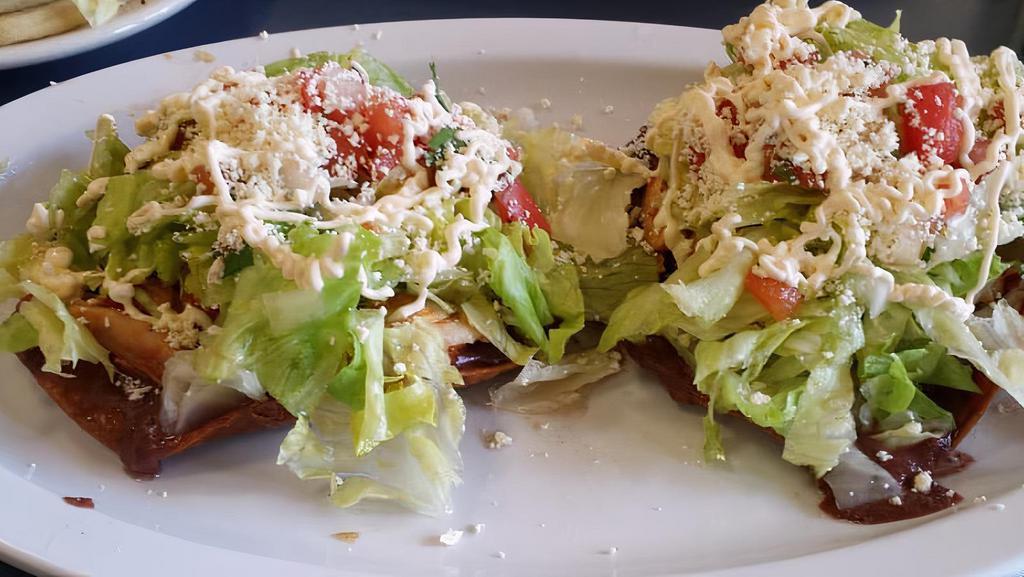 Tostadas De Pollo/Chicken Tostadas · Fried tortilla pilled high with beans, chicken, lettuce, tomato, sour cream and grated cheese.