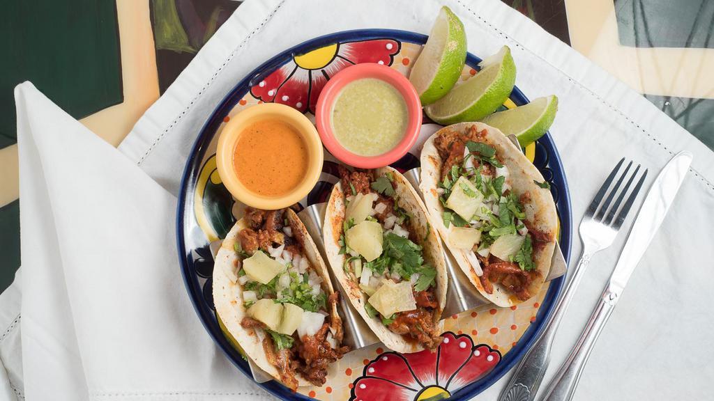 Tacos Al Pastor · Three tacos filled with marinated pork and fresh pineapple.