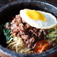 Dol-Sot Bi-Bim-Bap · Steamed rice topped with various cooked vegetables and a fried egg in a heated stone pot.