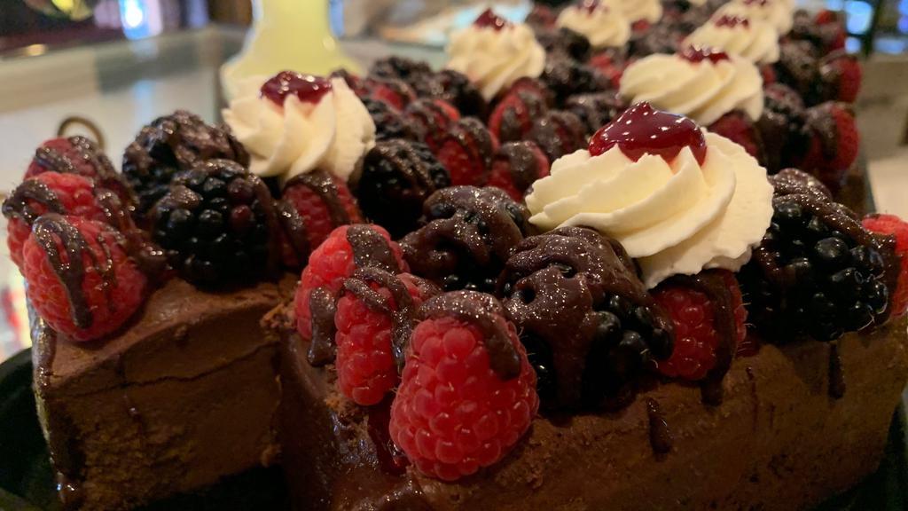 Chocolate Cheesecake Bar · A chocolate cheesecake bar with an Oreo crust, topped with raspberry puree, strawberries, black berries, and blueberries.
