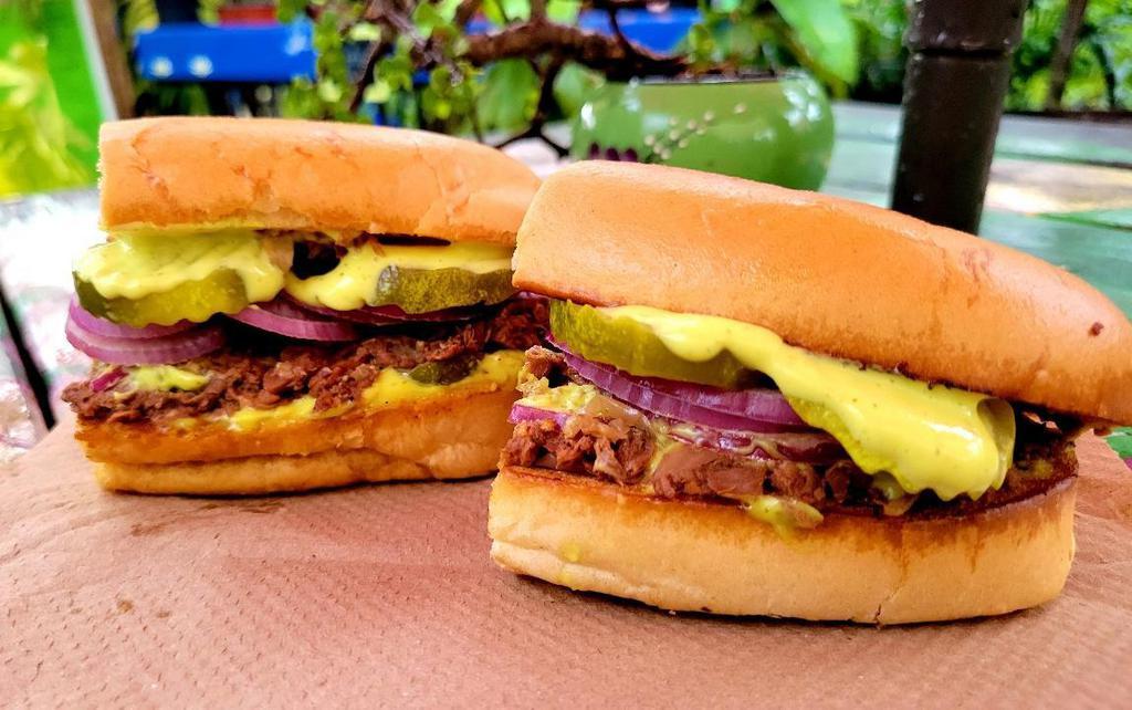 Vegan Pork Sandwich- Pan Con Lechon · Jackfruit Cooked with Cuban Mojo and onions, Topped with Raw Onions and Pickles. Served on Toasted Vegan Cuban Bread and Mojo Mayo. Served with Plantain Chips.. Contains gluten. For gluten free option add Gluten Free Burger Bun
