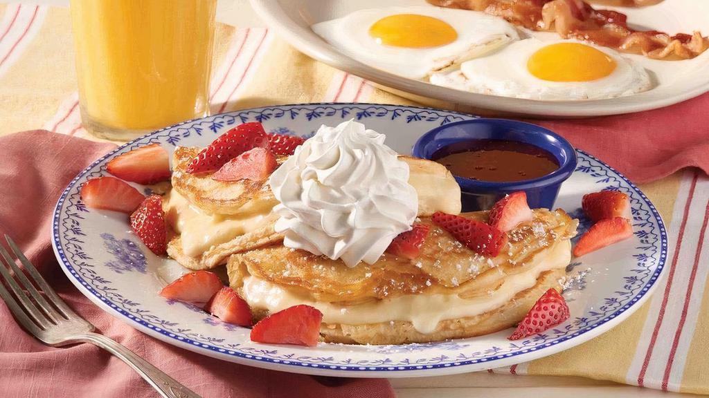 Stuffed Cheesecake Pancake Breakfast · Our classic homestyle buttermilk pancakes stuffed with creamy cheesecake filling and topped with fresh seasonal fruit, powdered sugar and served with strawberry syrup. Comes with two eggs plus choice of Thick-Sliced Bacon or Smoked Sausage.