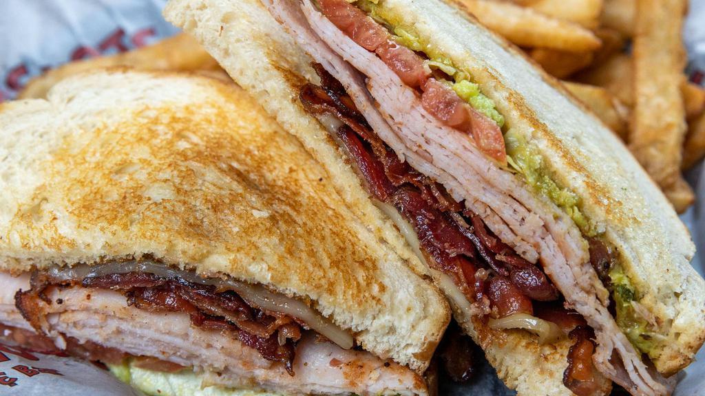 Turkey Club Sandwich · Grilled smoked turkey breast, hickory smoked bacon, pepper jack, guacamole, lettuce and tomatoes served on a toasted sliced sourdough bread.