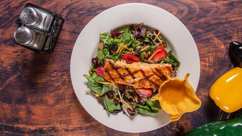 Grilled Salmon Salad · Salmon fillet on a bed of spring mix seasonal greens, and dried cranberries, toasted almonds, fresh strawberries, and shredded cheese. Topped with crispy corn tortillas strips, garnished with our mango vinaigrette.