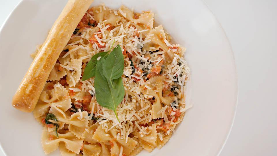Pomodora Pasta · Farfalle pasta and ripe Roma tomatoes meet a delightfully creamy wine-garlic sauce accompanied by sauted spinach and basil. Garnished with a medley of Parmesan and Romano cheeses.