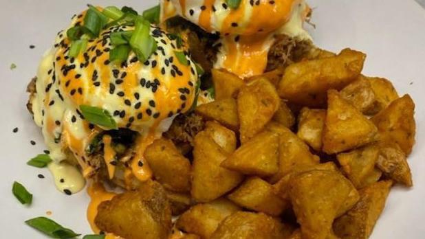 Korean Short Rib Benedict · Grilled baguette, 2 soft poached eggs, pulled short rib, kimchi, sriracha aioli, hollandaise, sesame seeds & scallions. Served with home fries.