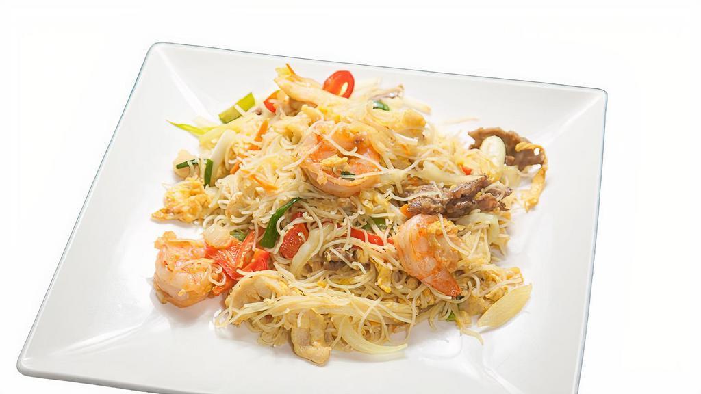 Singapore Curry Noodles · Stir-fried rice noodles with onions, bean sprouts, carrots, eggs, and toast in a yellow curry sauce, served with soup and a spring roll.