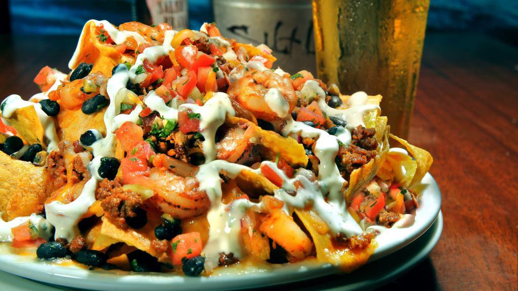 Shrimp & Chorizo Nachos · Contains bacon. Grilled shrimp and chorizo topped with corn, black beans, jack, and cheddar cheese, pico and finished with a cilantro lime cream drizzle.