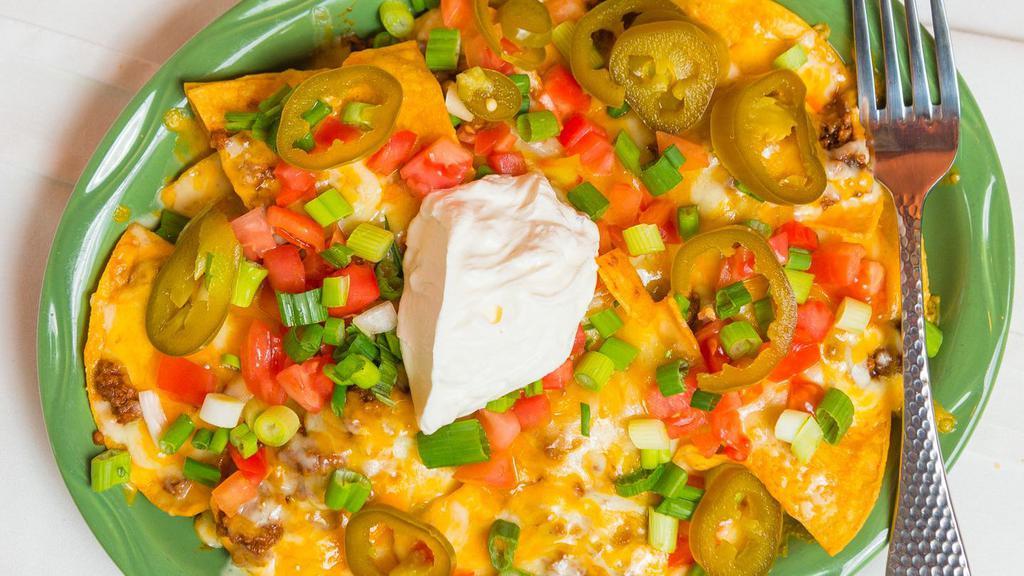 Grande Nachos · Crispy corn tortilla chips topped with melted jack and cheddar cheese, beans and your choice of ground beef, shredded beef or chicken topped with sour cream, tomatoes, green onions, and jalapeños.