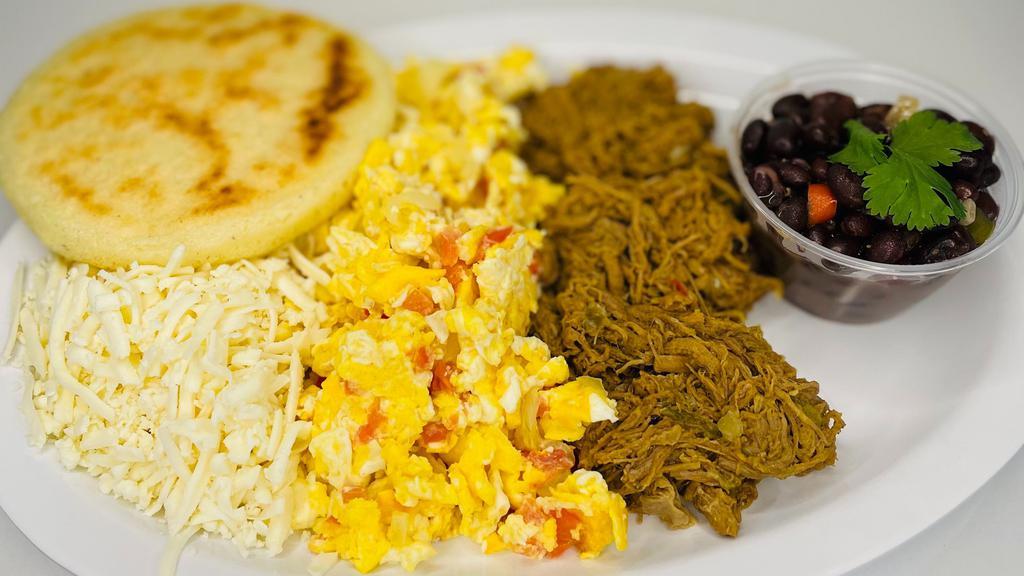 Desayuno Criollo · Scrambled eggs with tomatoes, onions, choice of shredded beef or chicken, black beans, shredded white organic cheese, arepa.