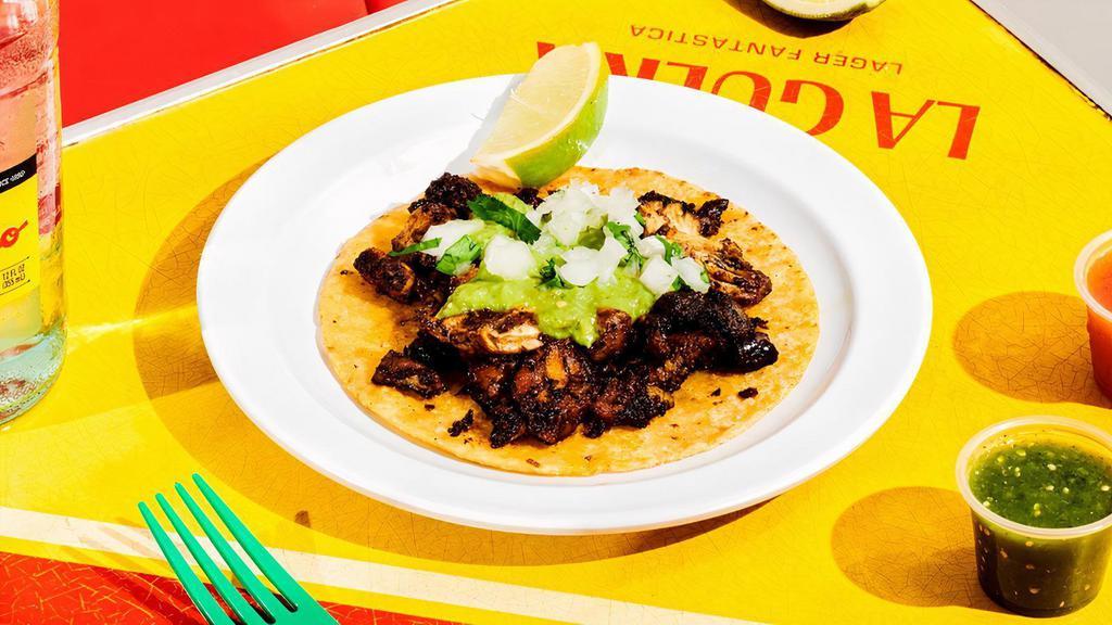 Pollo Yucateco Taco. · Free-range roasted chicken marinated in spicy recado rojo paste made from achiote, dried chiles, roasted garlic and black pepper and served with frijoles refritos, topped with cilantro, onions and avocado-tomatillo salsa.
