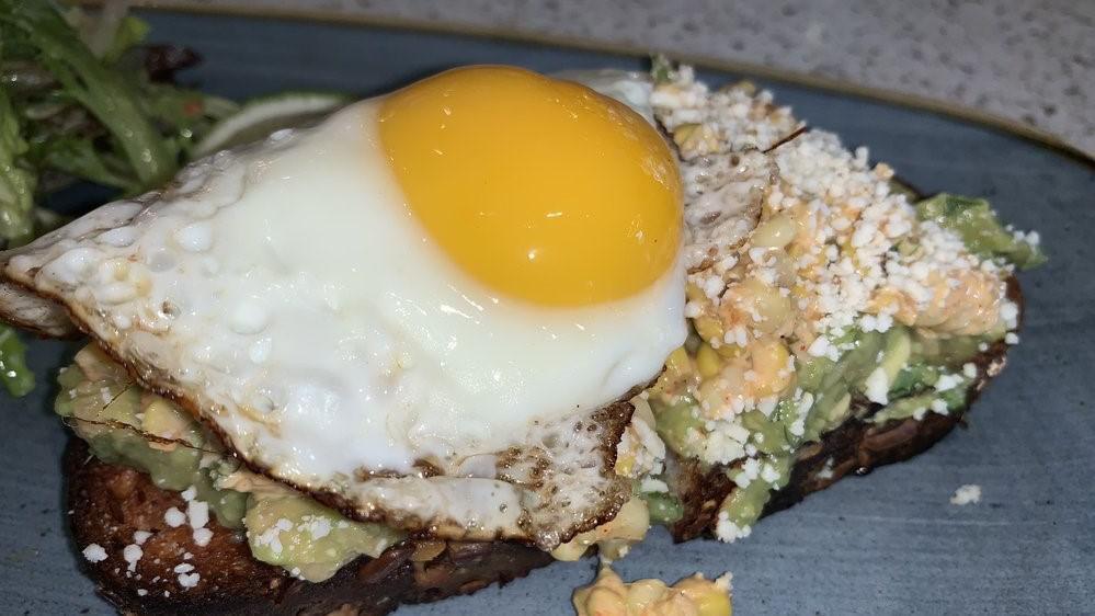 Avocado Toast With Egg · Avocado, Grilled Corn, Cotija Cheese, Spicy Mayo, Pickled Peppers, Cilantro, Multigrain Bread, Sunny Side Up Egg