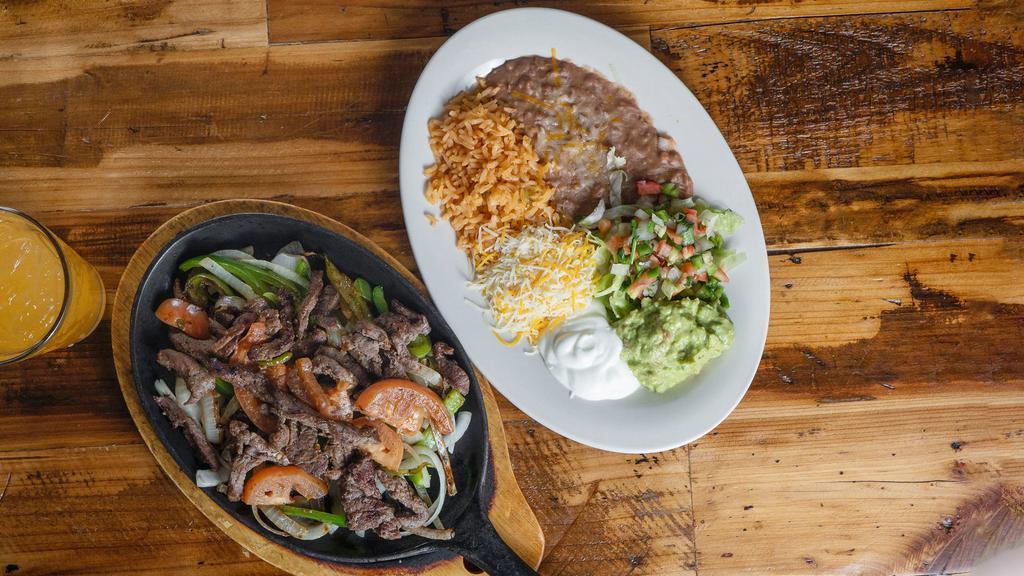Steak Fajitas · Marinated steak grilled with onions, bell peppers and tomatoes. Served with a side plate of rice, beans, Pico de gallo, lettuce, tomato, cheese, guacamole and tortillas.