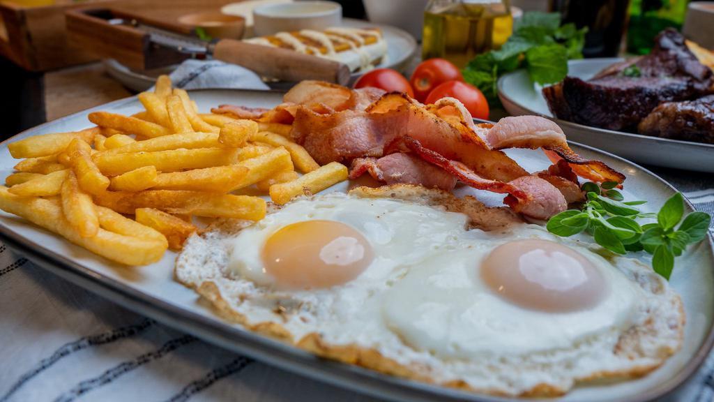 American Breakfast / El Americano · 3 bacon stripes and two fried eggs. All breakfasts include two sides: coffee or hot chocolate and toast, French fries or house potatoes.