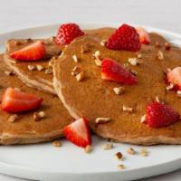 Fruit & Nut Multigrain Pancakes · Three multigrain pancakes with bananas and topped with fresh strawberries and pecan pieces.